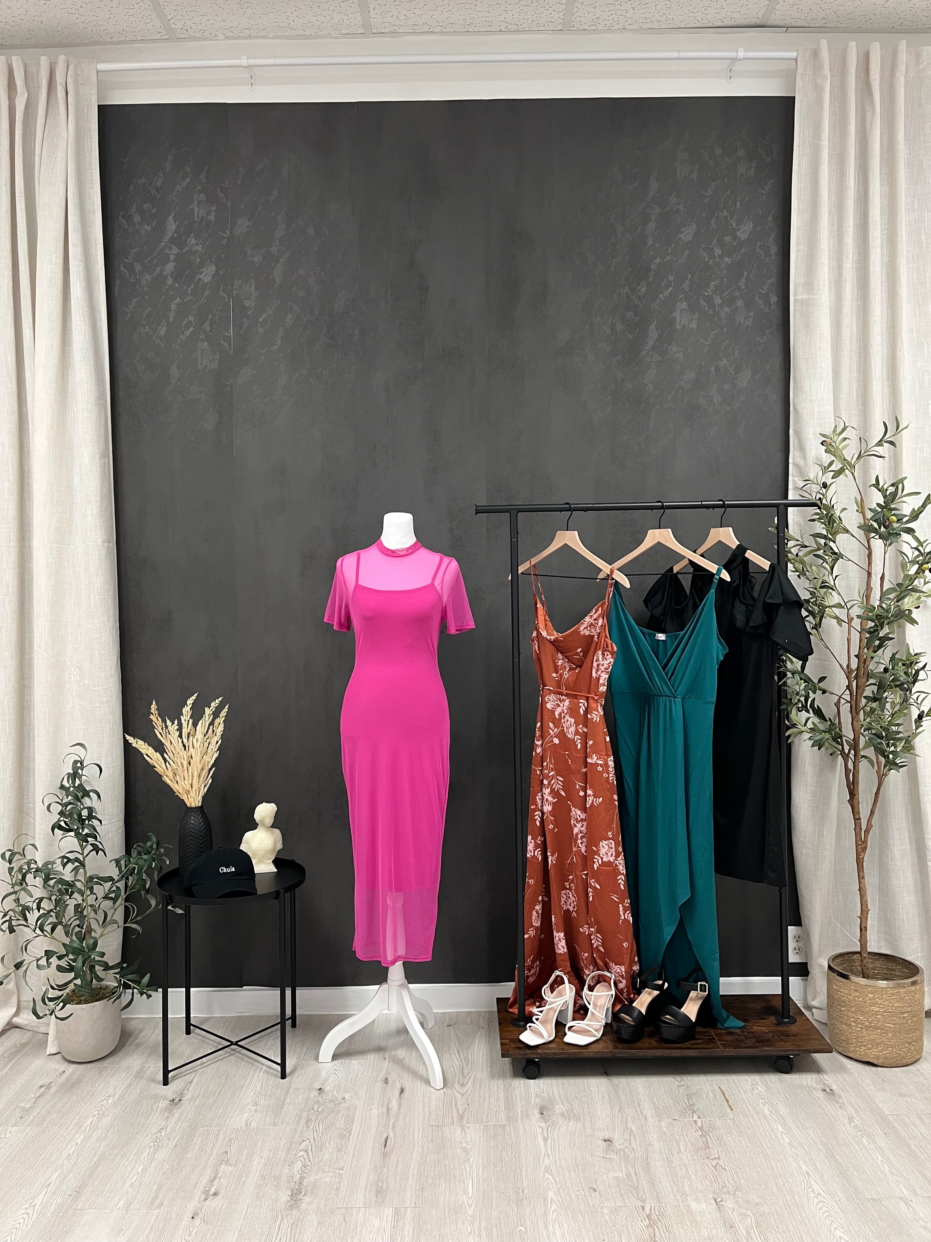 Various dresses hanging on a clothing rack. A pink dress, rust floral dress, green dress, and black dress.