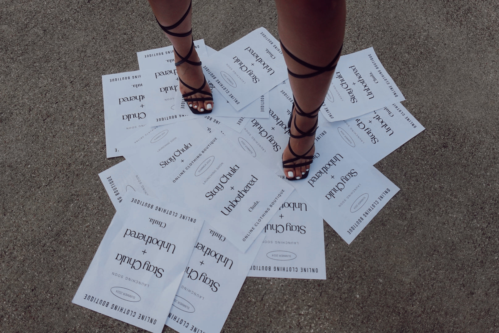 Strappy black heels standing on a pile of papers saying "Stay Chula + Unbothered"